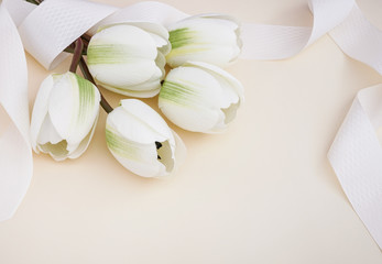 Beautiful fake white tulips draped in ribbon in pastel background. Concept for Mother's Day celebration with copy space.