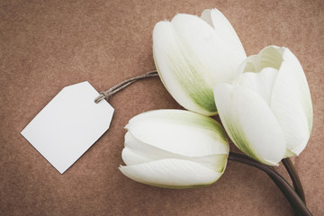 Artificial white tulips with greeting card in kraft paper background. Concept for Mother's Day with copy space.