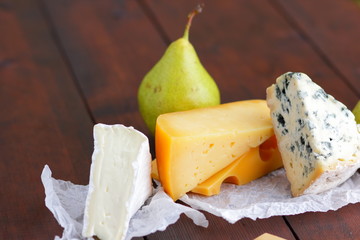 Cheese and pear on wooden boards. Various cheese on natural blurred background. Dorblu, camembert...