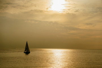 Sunset in the sea, a small sailing boat at sunset away - 250116680