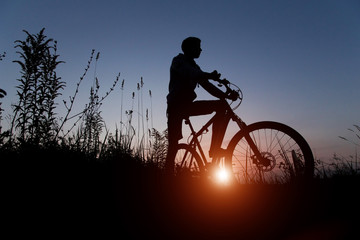 Obraz premium Silhouette of cyclist on bicycle at sunset sky background with sun and sunlight, copy space