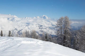 Snow covered trees and Mont Blanc mountain above clouds. View from the French alpine ski resort La Plagne