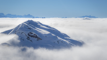 Mountain peaks covered in snow above clouds in La Plagne, French Savoy Alps. Winter scenic scenery, blue sky and stunning views.