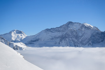 Mountain peaks covered in snow above clouds in La Plagne, French Savoy Alps. Winter scenic scenery, blue sky and stunning views.