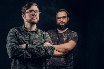 Two clever bearded hacker posing on camera crossed arms in a studio on a black background