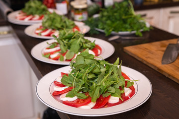 Plates with tomatoes, mozzarella and Basil on the serving kitchen table