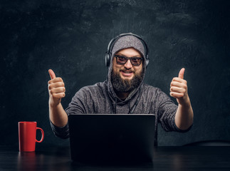 Satisfied hacker sits behind a laptop in a dark office