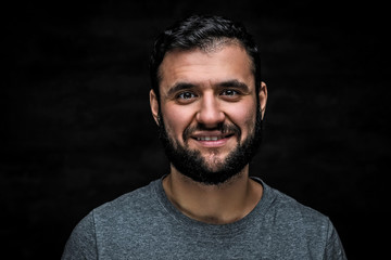 Fototapeta premium Close-up portrait of a cheerful bearded man, isolated on a dark background.
