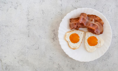 Fried heart-shaped eggs with bacon on a plate, top view, copy space. Breakfast for lovers, concept for Valentine's day.