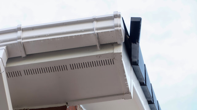A damaged side roof panel on a house beside modern uPVC guttering, downpipe and soffit.
