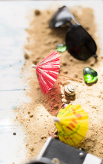Beach still life. Black glasses with cocktail umbrellas, seashell on sand on a wooden background
