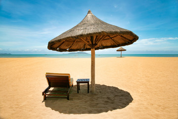 Lonely chaise longue and table, standing on a deserted beach under umbrellas of palm leaves. Sanya, Hainan