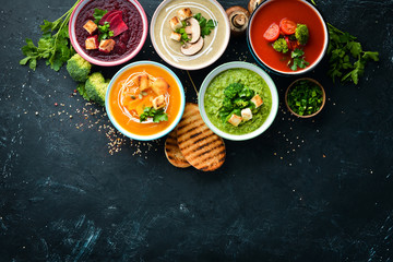 Assortment of colored vegetable cream soups. Dietary food. On a black stone background. Top view. Free copy space.