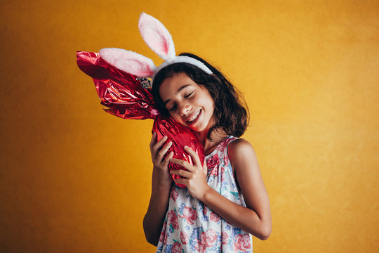 Cute little child wearing bunny ears on Easter day on color background. Girl holding chocolate easter egg