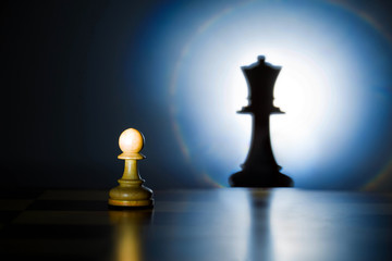 A pawn on a chessboard looks at its shadow of the future queen - obrazy, fototapety, plakaty