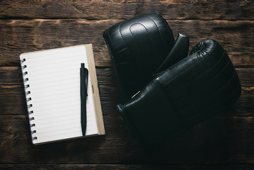 Blank notepad with empty sheets for boxing exercise list and boxing gloves on a brown aged wooden...