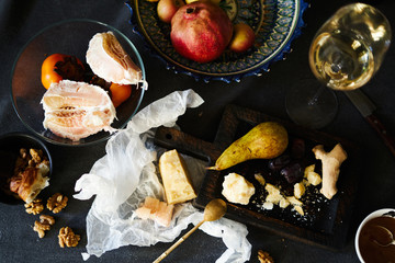 Still life on dinner table with cheese pieces, pear, white wine, walnut, pomelo on wooden board.