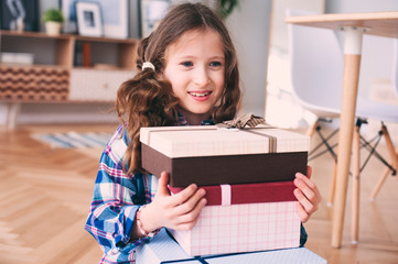 happy kid girl preparing or getting many gifts for birthday. Child with stack of gifts at home