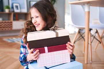 happy kid girl preparing or getting many gifts for birthday. Child with stack of gifts at home