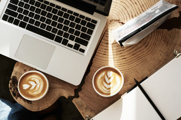 Opened laptop and two cup of coffee with flower decoration on top, view from above, wooden slab table.