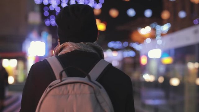 Unrecognizable man talks with his friend by smartphone in the night city, slowmotion, rear view