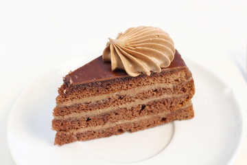 A piece of delicious chocolate birthday layer cake dessert with chocolate cream decoration on a white plate meny style