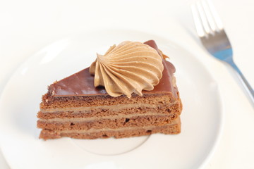 A piece of delicious chocolate birthday layer cake dessert with chocolate cream decoration on a white plate meny style