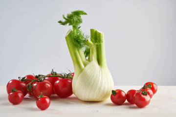 Fresh fennel and red tomato on bright wooden background. Concept of healthy food and nutrition.