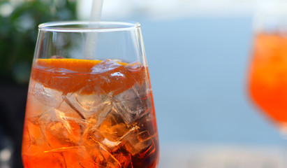 Iced bright orange drink with straw, orange peel and ice cubes in transparent glass. Selective focus