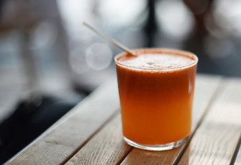 Healthy orange fruit and vegetable smoothie with straw on wooden table. Selective focus