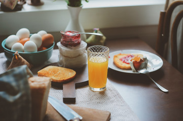 country cottage kitchen with breakfast on wooden table. Toast with jam, farm eggs and coffee