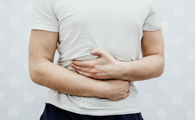 Abdominal pain, stomach problems. A man is holding his hands behind his belly on a light...