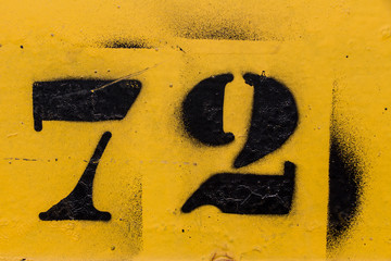 black number stencil painted on yellow background, number 72, number seventy two