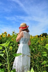 Naklejka premium Rücken eines Mädchen mit Strohhut im Sonnenblumen Feld mit blauem Himmel