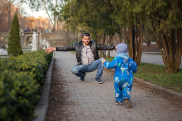 Father and little son having fun together: Little toddler boy runs to his father in the spring park, dad is ready to embrace his son