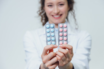 The young doctor's daughter is on a gray background. During this, pills hold close-up portrait. Two blister packs with pills.