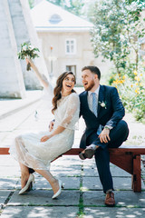 Stylish and beautiful wedding couple sitting on the bench and having fun