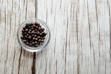 Juniper berries on a wooden table in a bowl. Juniper on the table. The concept of using seasonings for dishes. Eating spiced dishes.