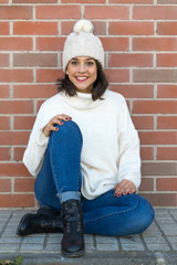 pretty young girl with hat and white winter sweater on brick wall