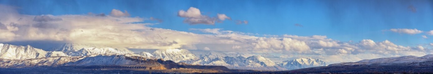 Obraz premium Winter Panoramic view of Snow capped Wasatch Front Rocky Mountains, Great Salt Lake Valley and Cloudscape from the Bacchus Highway. Utah, USA.