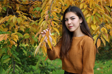 beautiful girl with dark hair and blue eyes in a yellow sweater in the autumn forest