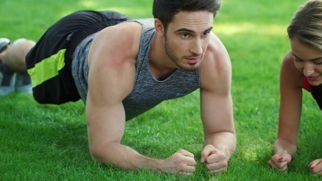 Fitness couple training plank workout giving five after finish in summer park
