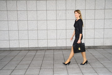 businesswoman with briefcase, walking in front of a wall