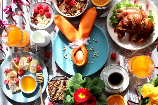 Breakfast food table. Festive brunch set, meal variety with pancakes, croissants, juice, fresh berries, granola and fresh fruits. Easter breakfast. Top view with copy space.