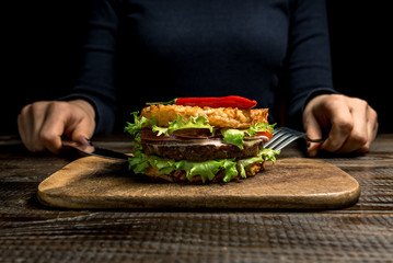 Healthy lifestyle, proper nutrition. Female hands are holding cutlery over a useful rice burger with vegetables, herbs and cutlet on a wooden board