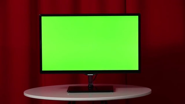 Flat screen TV. Standing on a white table. Green screen. Top secret. Red background.