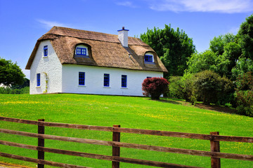 Traditional thatched roof cottage house in rural Ireland with green lawn under blue skies
