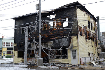 A burned building on a street corner in winter. The building is completely burned and looks like it will colapse.