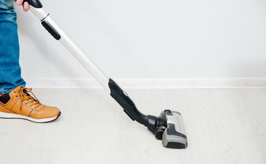 The man is vacuuming in the apartment. A man uses a vacuum cleaner to clean the apartment. Concept of caring for the interior of the apartment, cleaning. Help husbands in housekeeping.