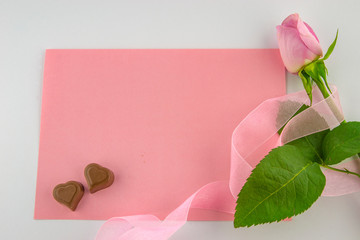 International Women's Day, March 8. Blank pink card with a pink rose wrapped in a decorative pink ribbon and two chocolate-shaped hearts on a white background.